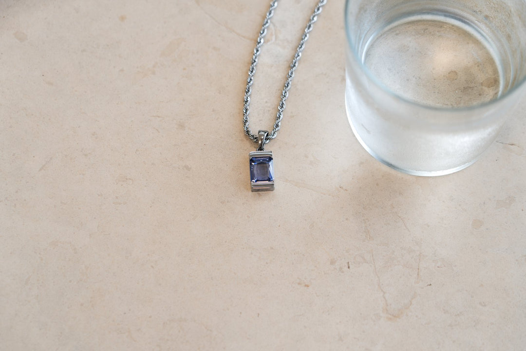 Silver Chip Tanzanite pendant on a 3mm rope chain lying on a stone table next to a glass of water