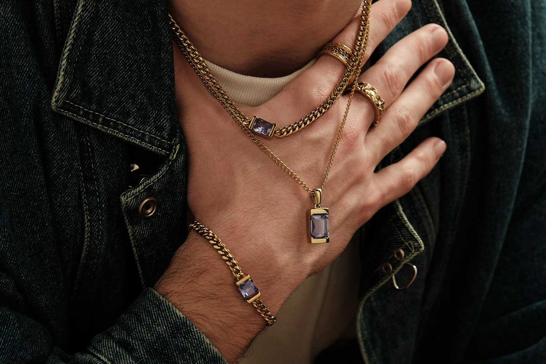 Man in a denim jacket wearing a gold Cuban chain layered over a pendant chain, two stacked gold rings and a gold Cuban bracelet